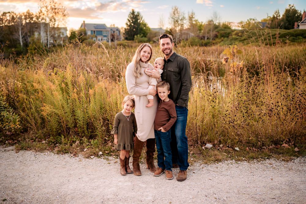 A family of three poses together on a gravel path during sunset in autumn.
