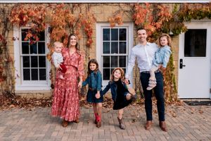 A family poses in front of a brick building covered in autumn ivy.