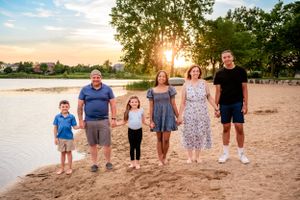 Family group stands together on sandy beach at sunset.