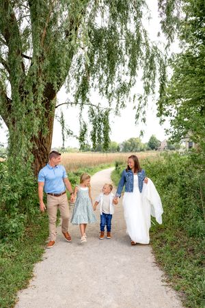 Family walking together on a dirt path surrounded by willow trees and tall grass on a sunny summer day.