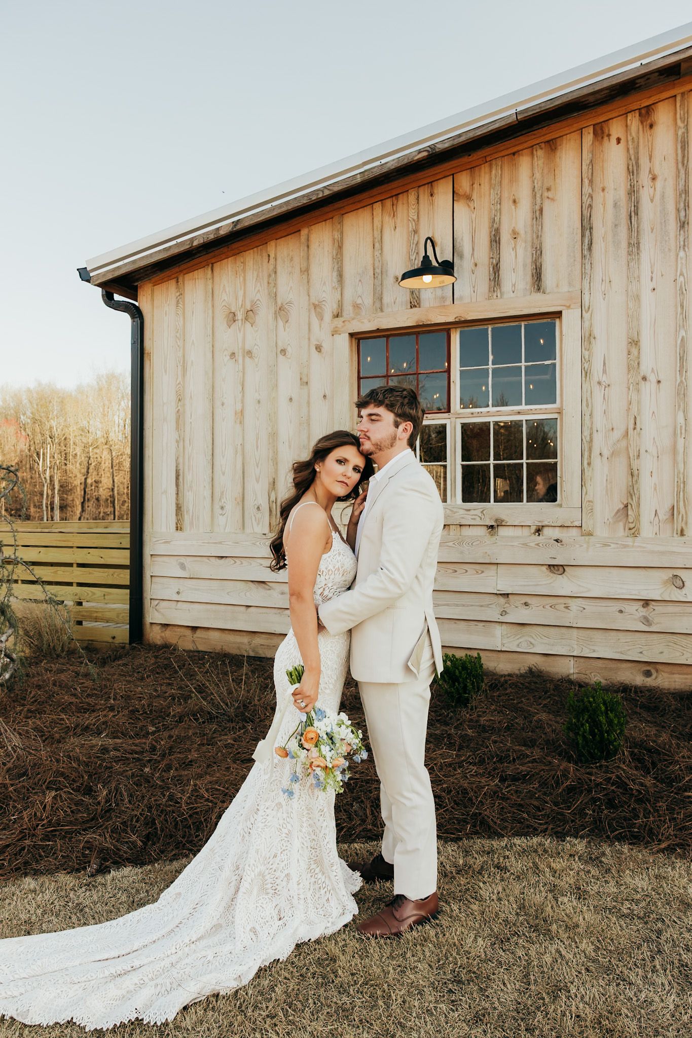 bride leaning on grooms chest in front of their barn wedding venue