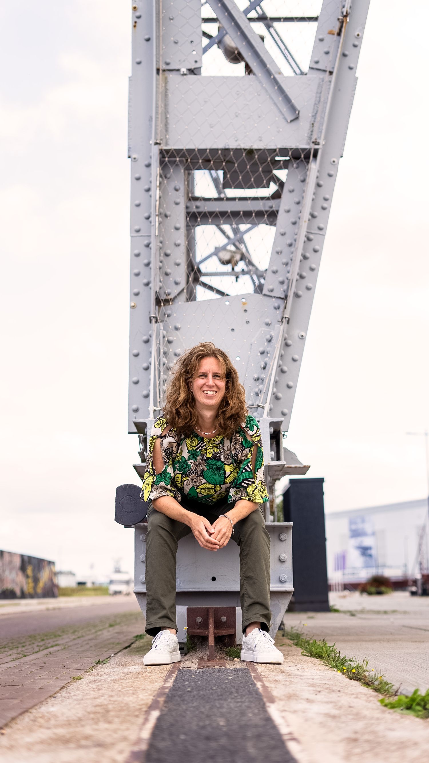 Person sitting under large metal bridge structure on sunny day.