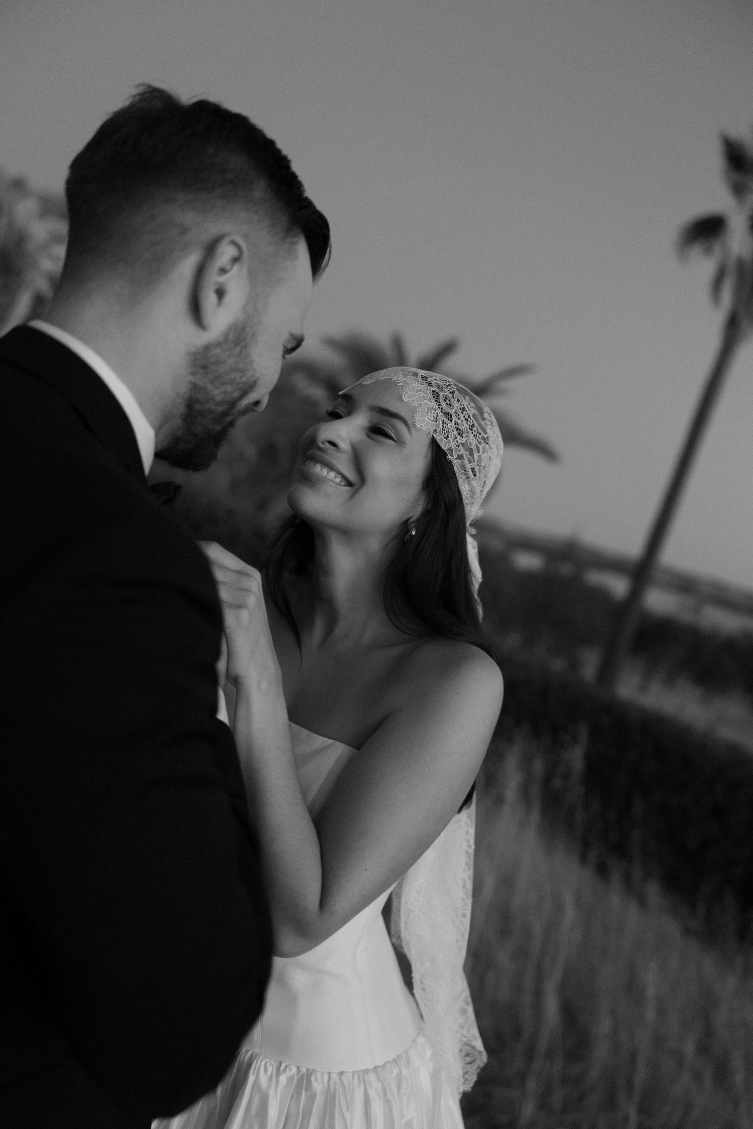 A romantic black and white wedding photo series showing a couple embracing and kissing against a palm tree backdrop.