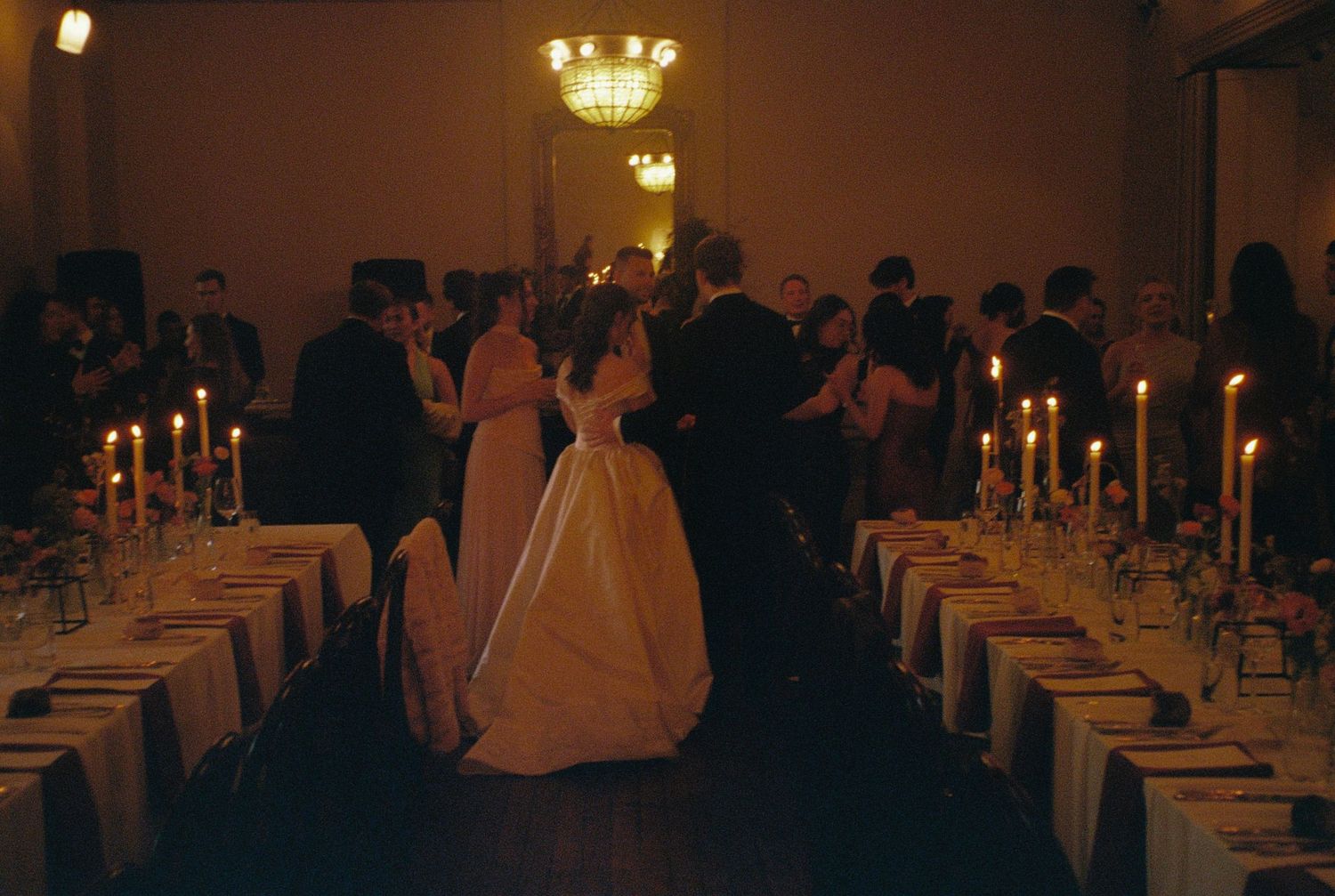 Bride and groom share first dance surrounded by candlelit tables and guests at an elegant wedding reception.