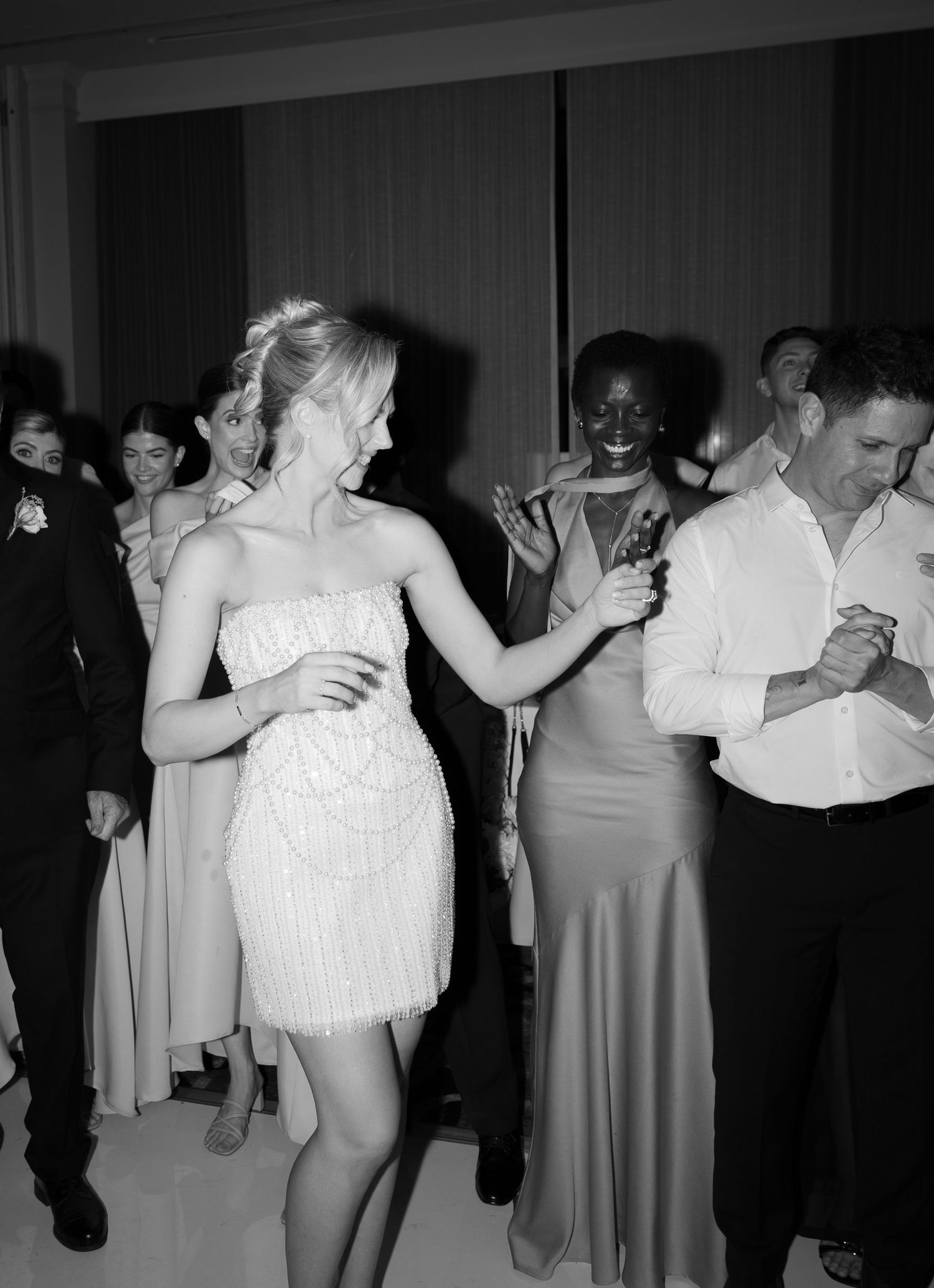 Wedding guests dance together in formal attire at an evening reception captured in black and white photography.
