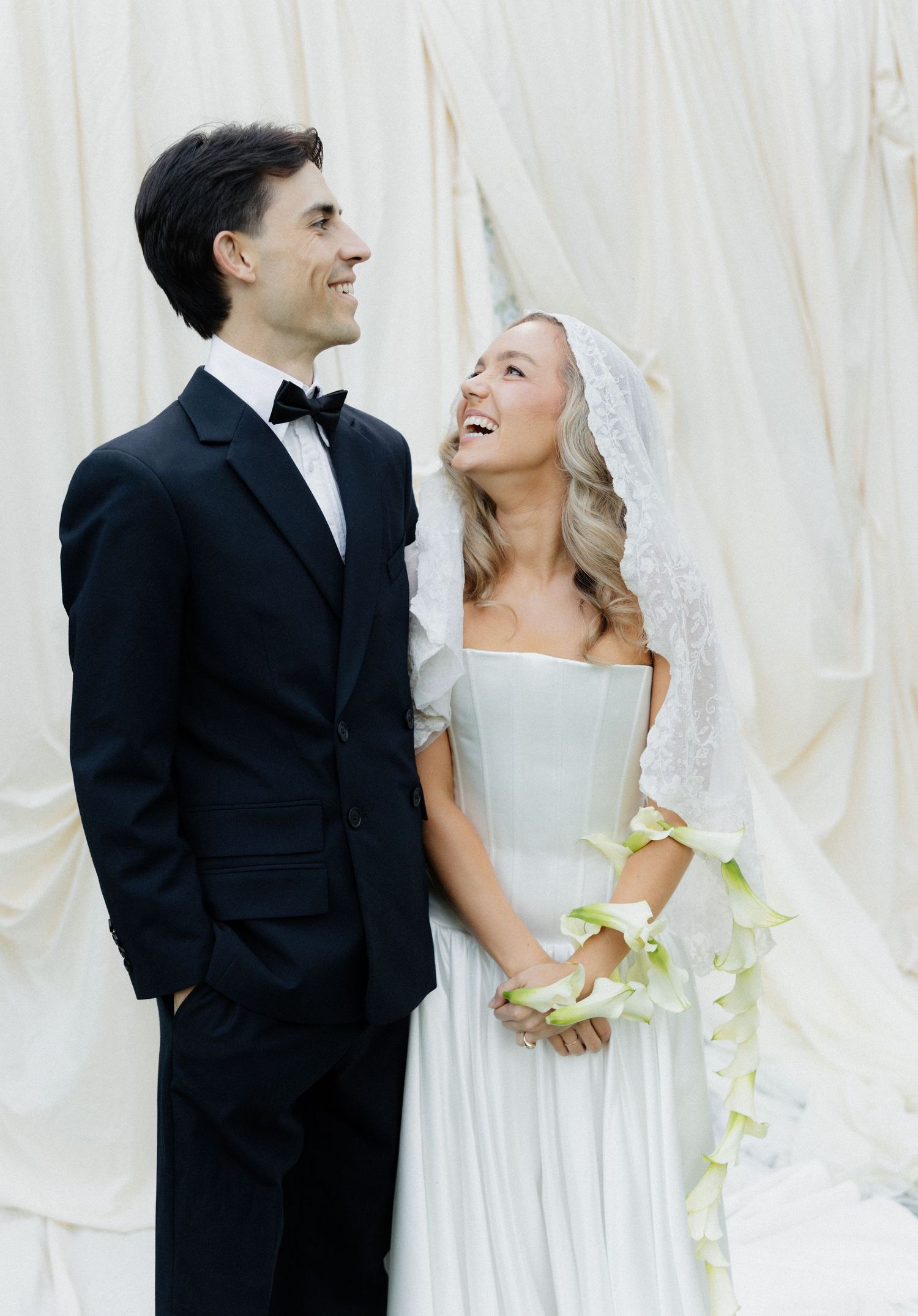 A romantic wedding couple in black and white formal attire share joyful moments against a light backdrop.