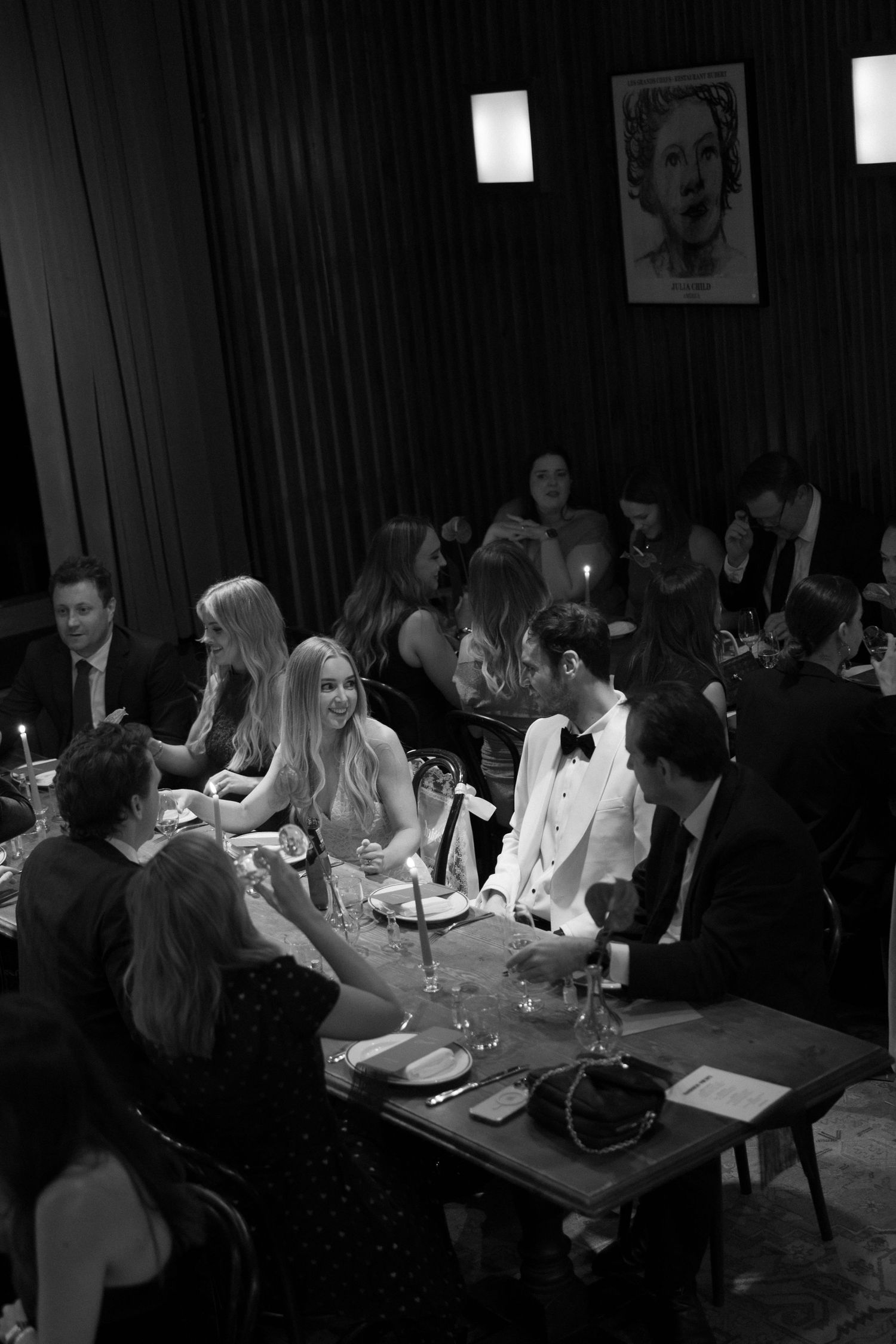 Black and white photo of elegantly dressed guests dining at a candlelit restaurant during a formal evening event.