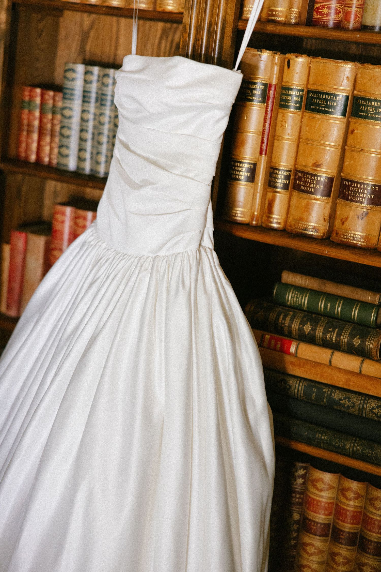 Classic white wedding dresses displayed in a vintage library setting with antique leather-bound books on wooden shelves.