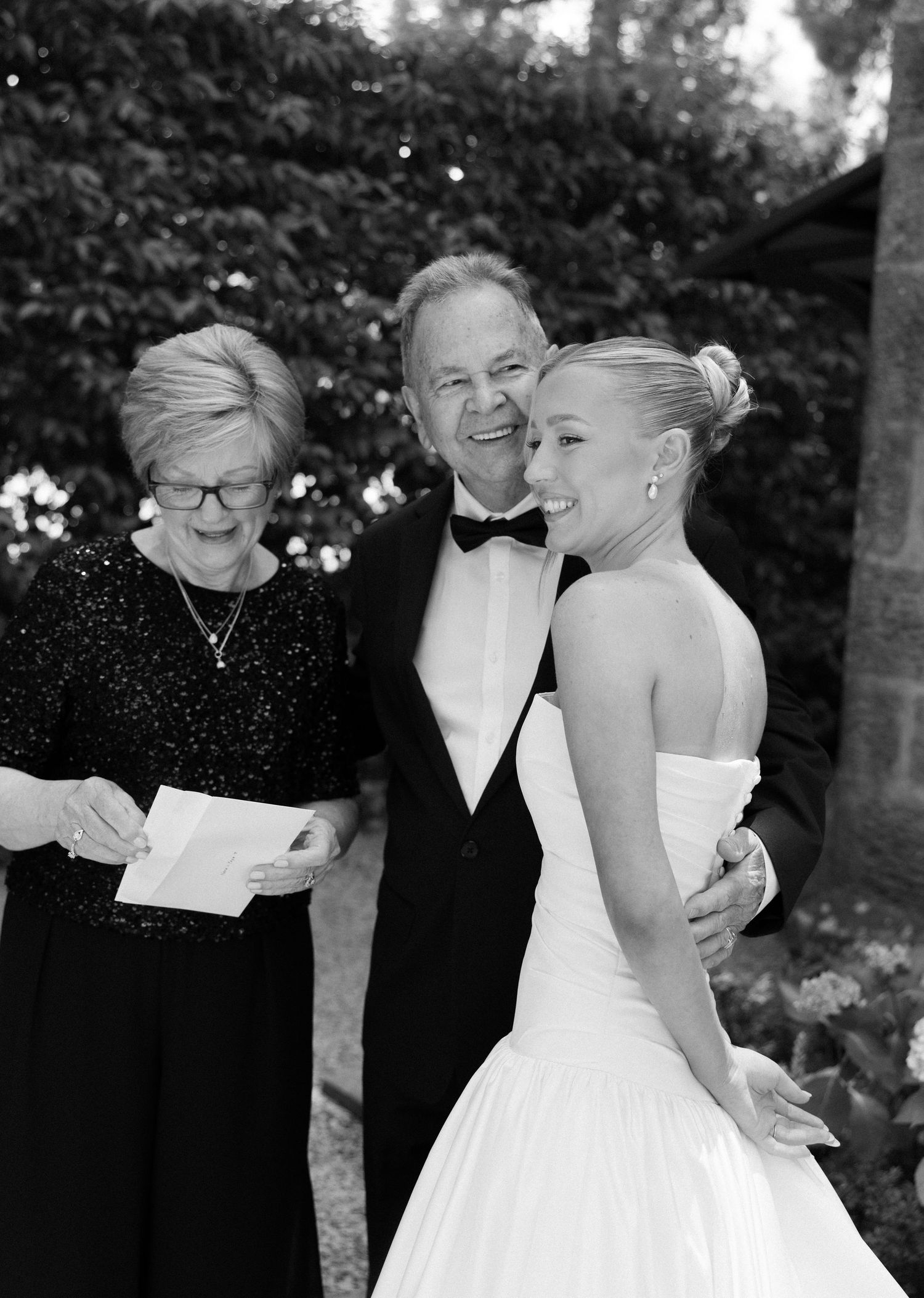 A series of black and white wedding photos showing a couple sharing intimate moments with loved ones outdoors.