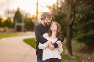 Happy couple embraces and laughs together on a pathway during golden hour sunset.