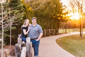 Couple walking together on a path through a park at golden hour sunset with a wooden fence in background.
