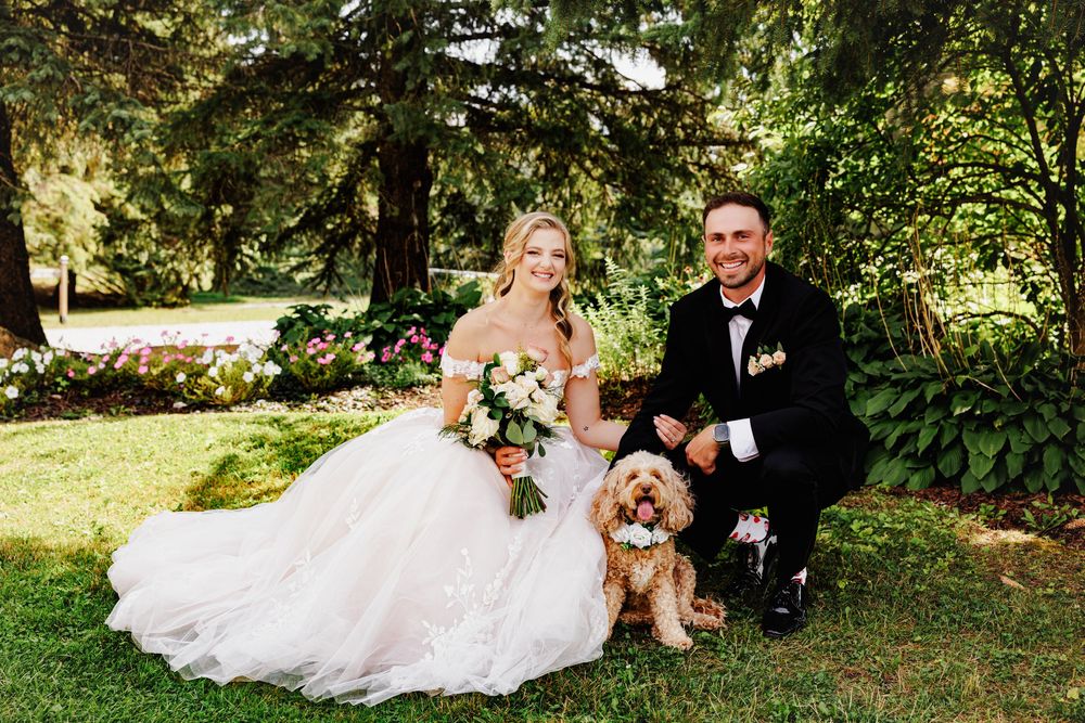 Bride and groom posing with their golden doodle dog in a lush garden setting on their wedding day.