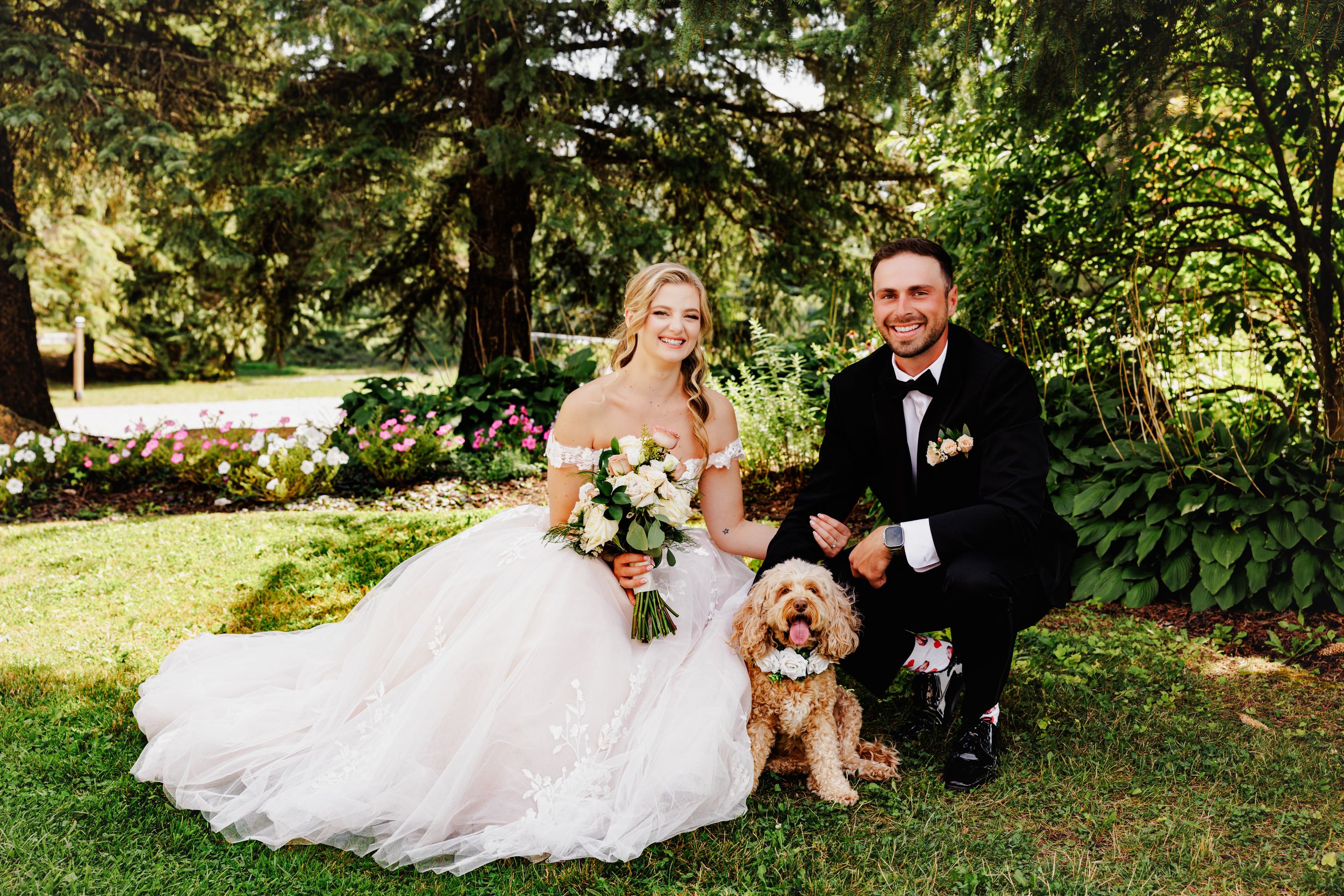Bride and groom posing with their golden doodle dog in a lush garden setting on their wedding day.