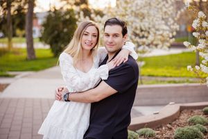 A couple poses together under blooming cherry blossom trees in a spring engagement photo session.