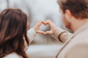Two people form a heart shape with their hands in soft lighting creating a romantic moment.