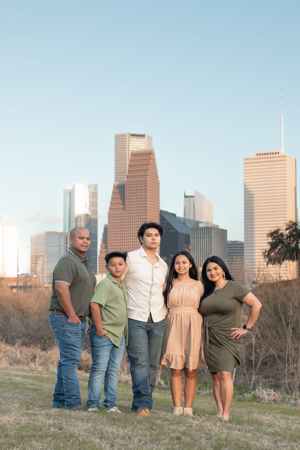 Family of five poses together on grassy hill with Houston downtown skyline in background.