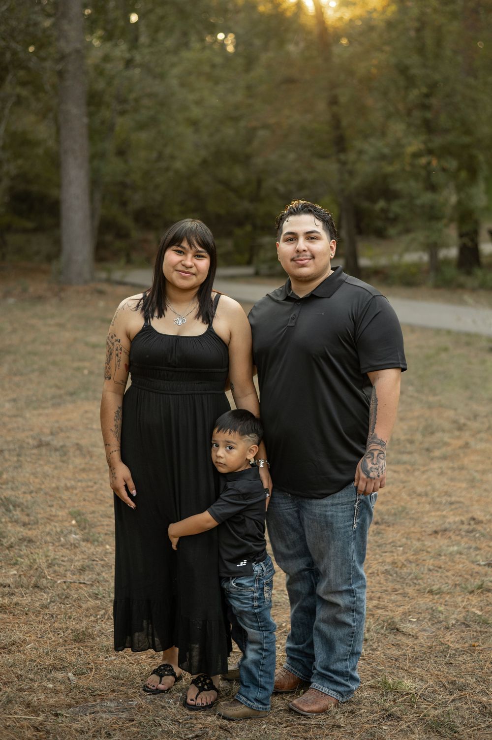 A family poses together at sunset in a wooded outdoor setting with golden sunlight filtering through the trees.