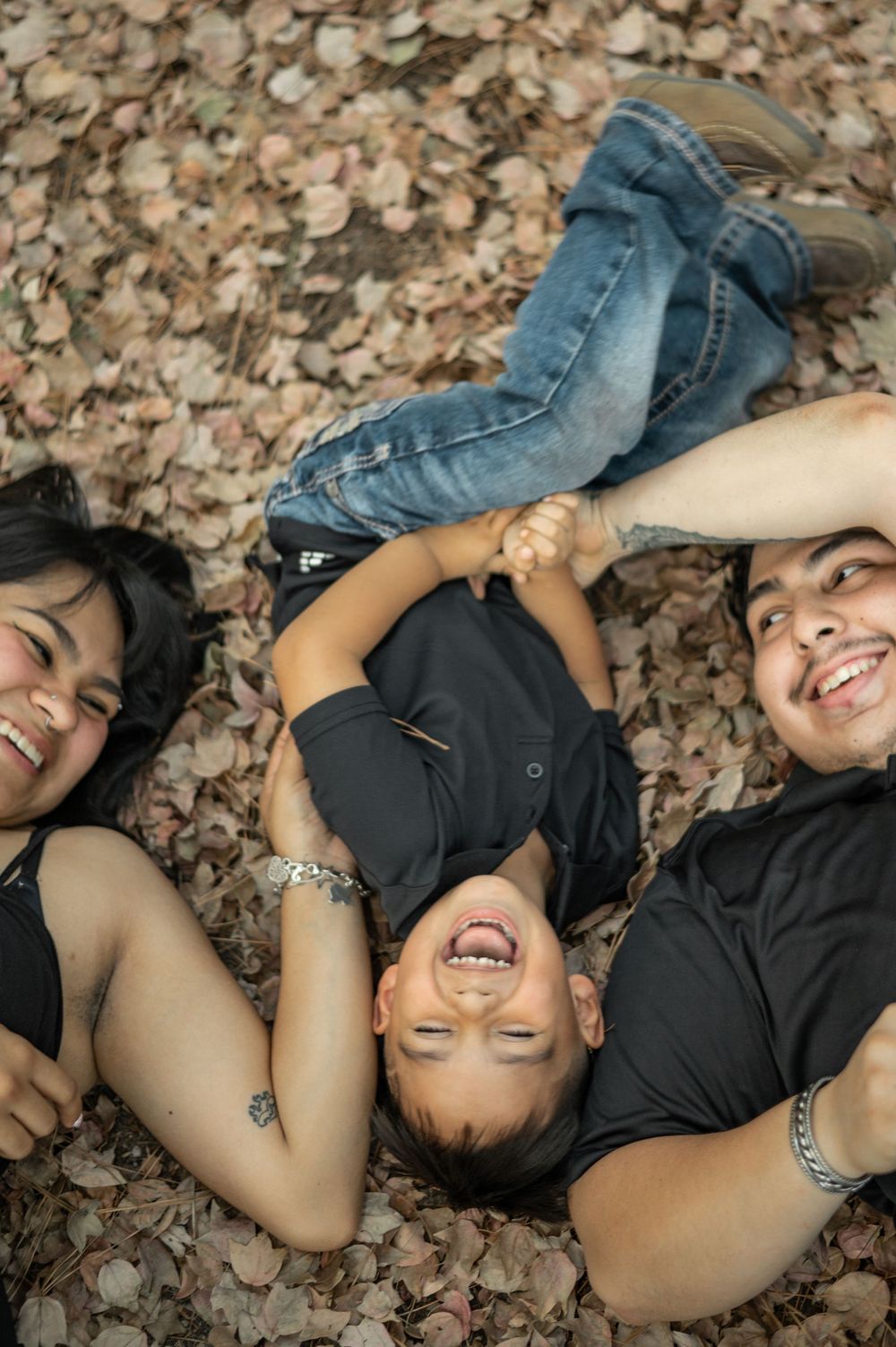 Family members lying on autumn leaves on the ground, sharing joyful laughter together.