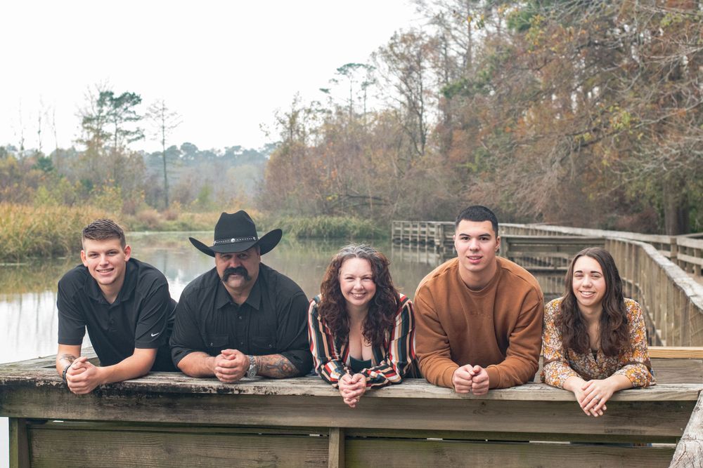 Friends leaning on wooden dock railing overlooking water in natural setting.