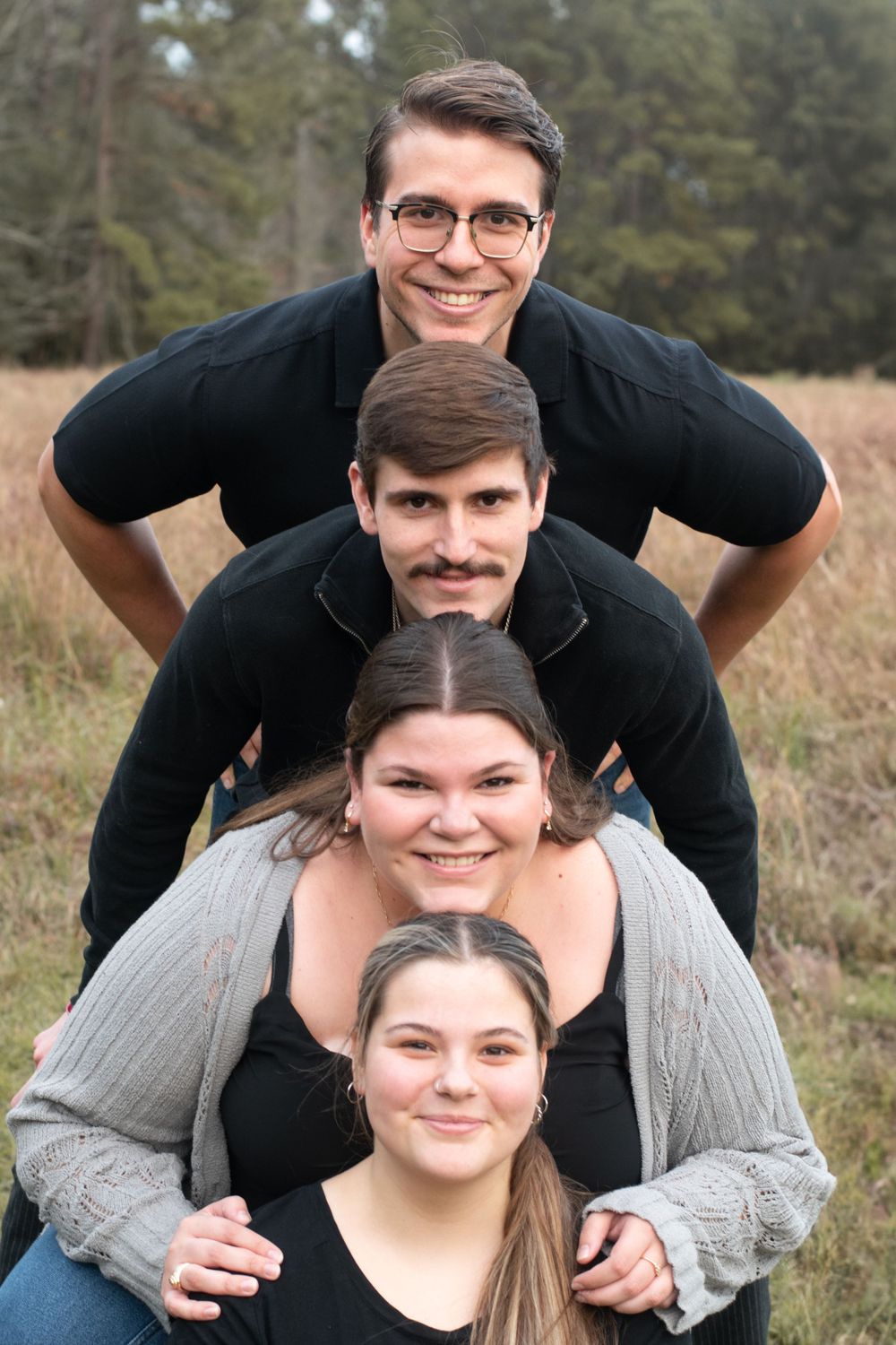 Playful group photo with four people stacked in pyramid formation outdoors.