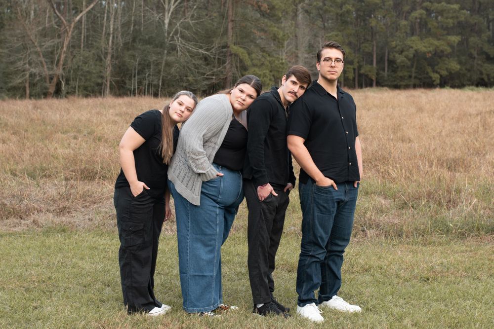 Group of four friends posing casually together in an outdoor field setting.