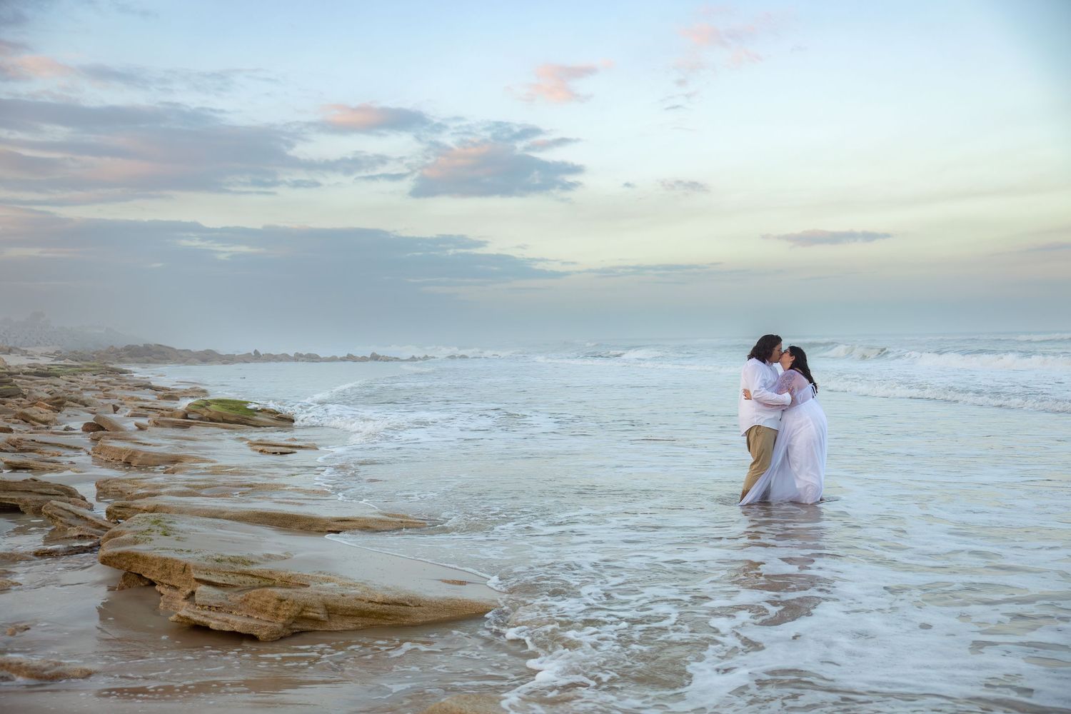 Romantic beach scene with couple standing in ocean waves at sunset.