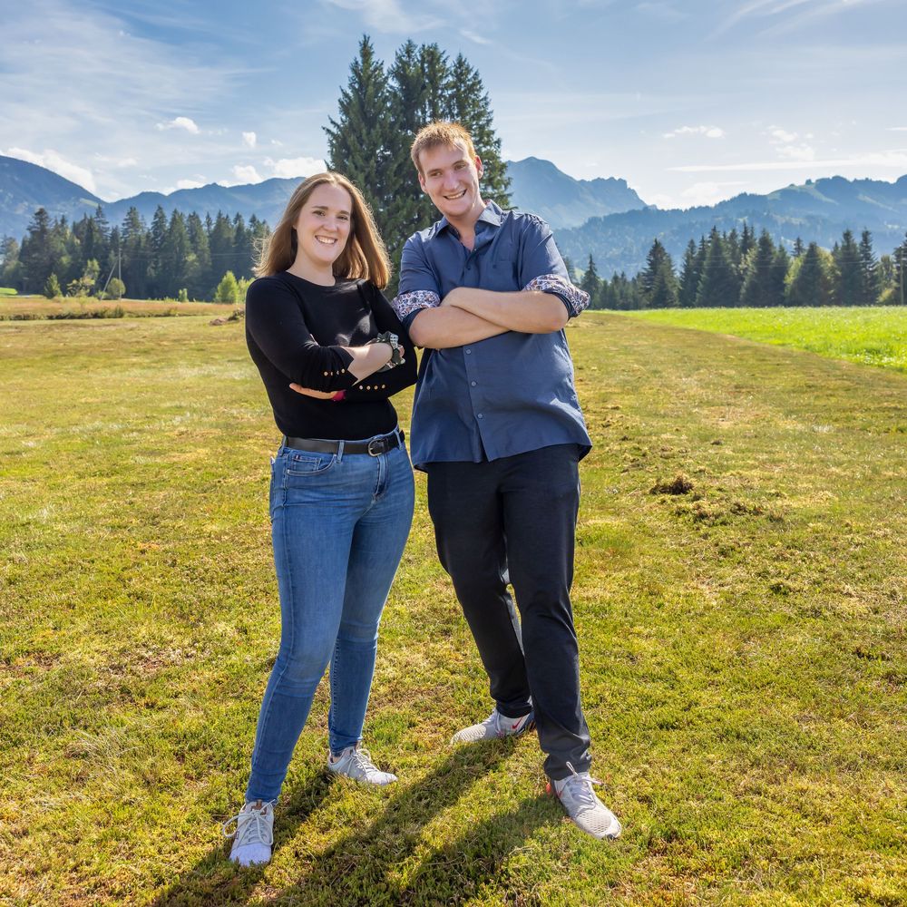 People enjoying a sunny day in an alpine meadow with mountains and evergreen trees in the backdrop.