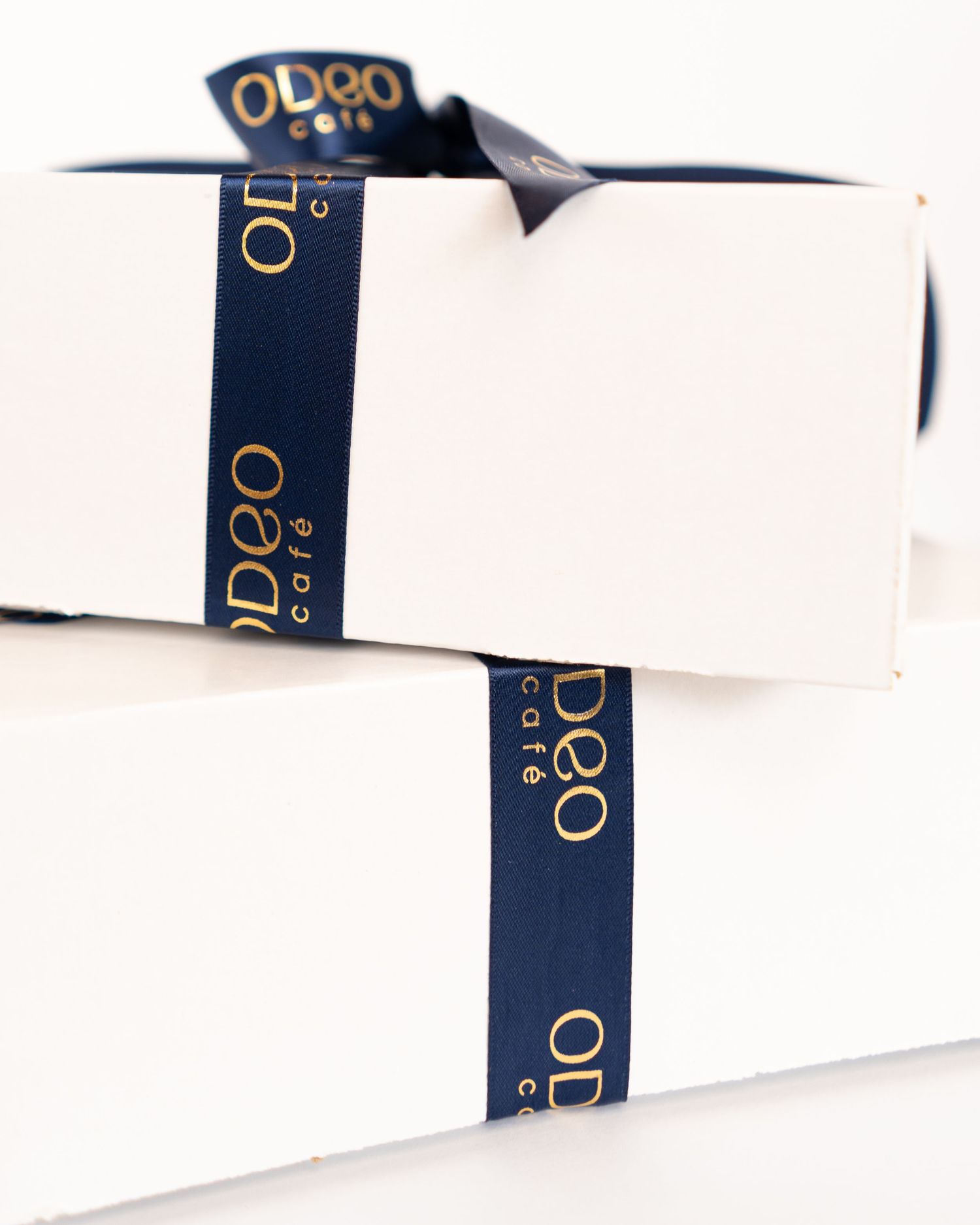 White gift boxes stacked with navy blue ribbon featuring gold text.