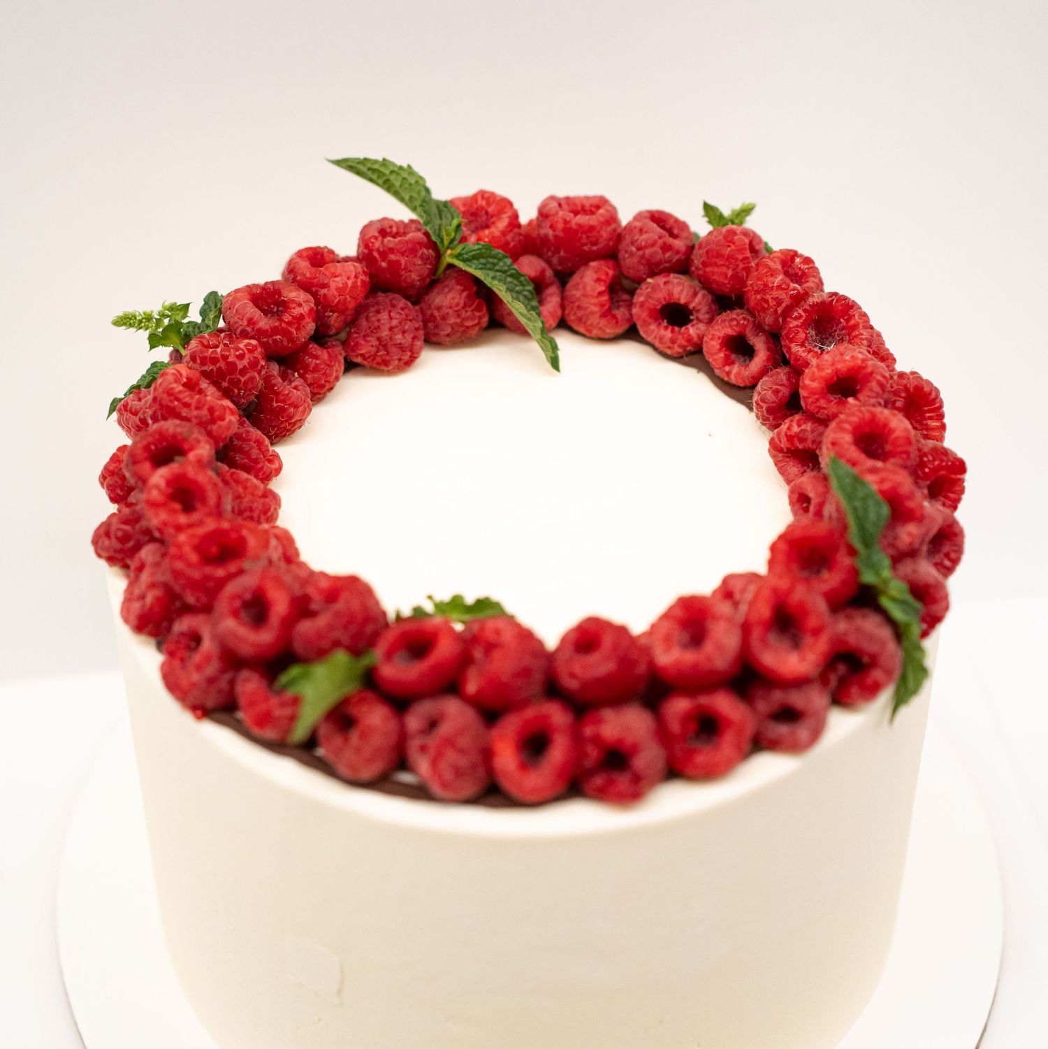 Elegant white cake decorated with fresh red raspberries arranged in a circular pattern on top.