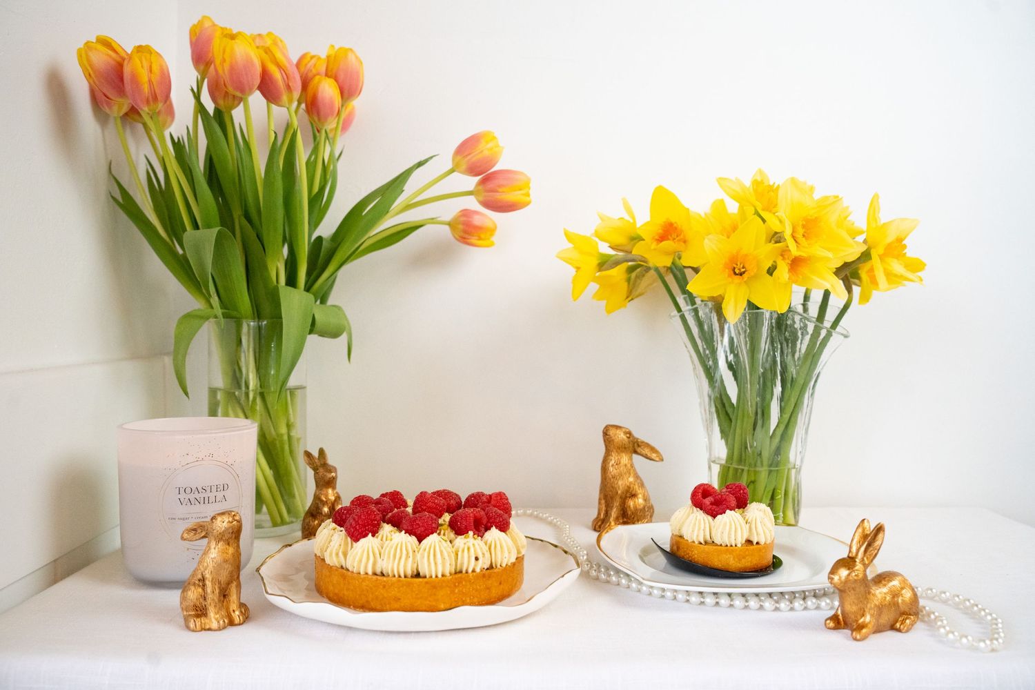 Spring table setting with orange tulips, yellow daffodils, and bunny decorations around a fruit-topped cake.