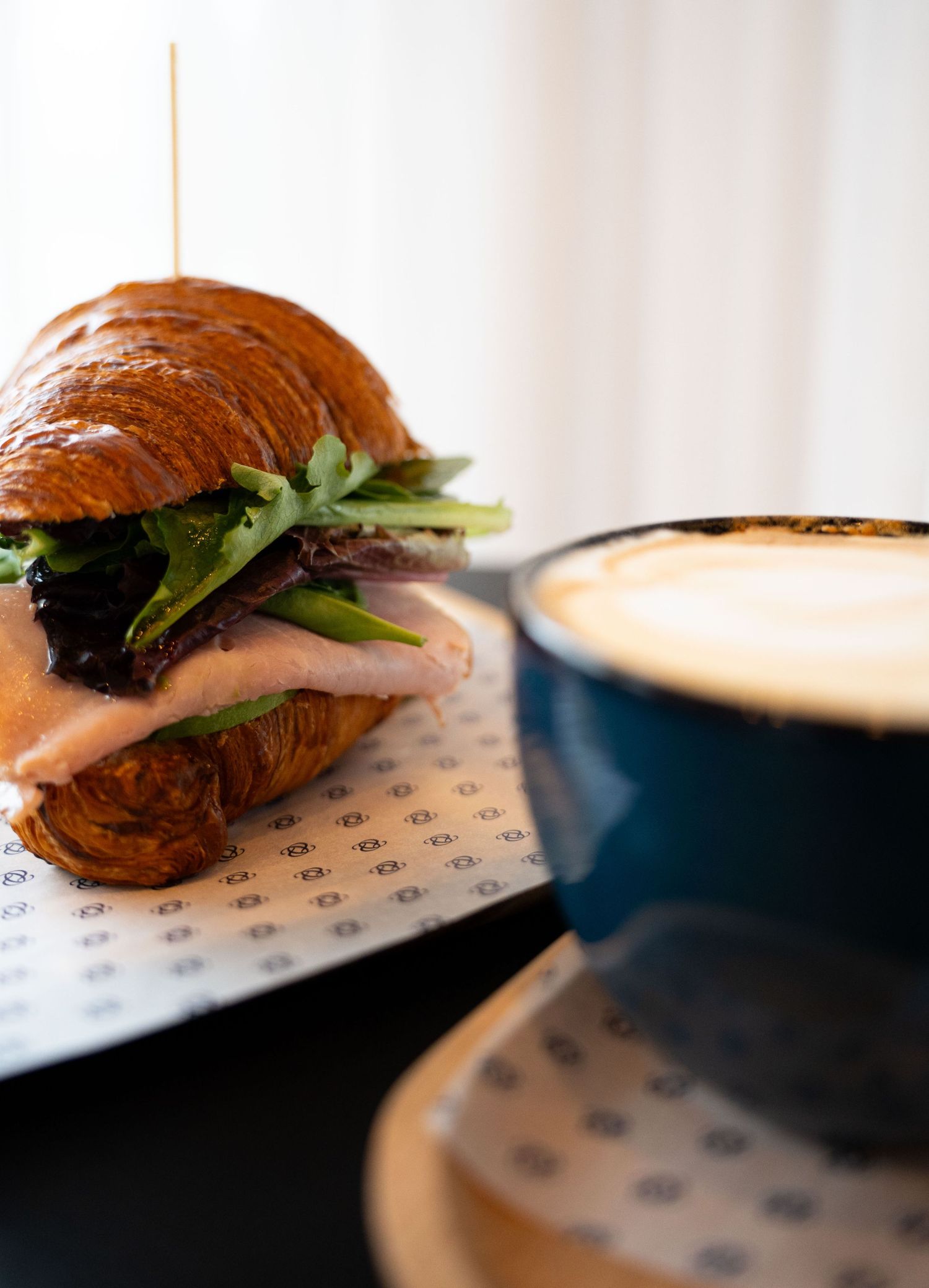 Gourmet croissant sandwich served with a cappuccino in a blue cup.