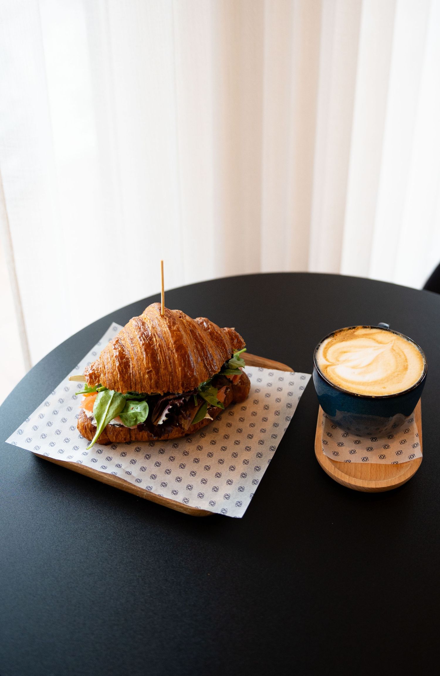 Artisanal croissant sandwich and latte coffee served on black table.