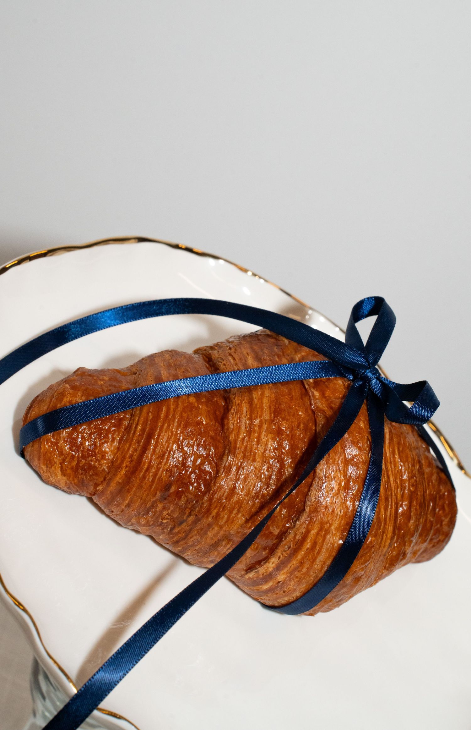 Golden brown croissant tied with navy blue ribbon on a white plate.