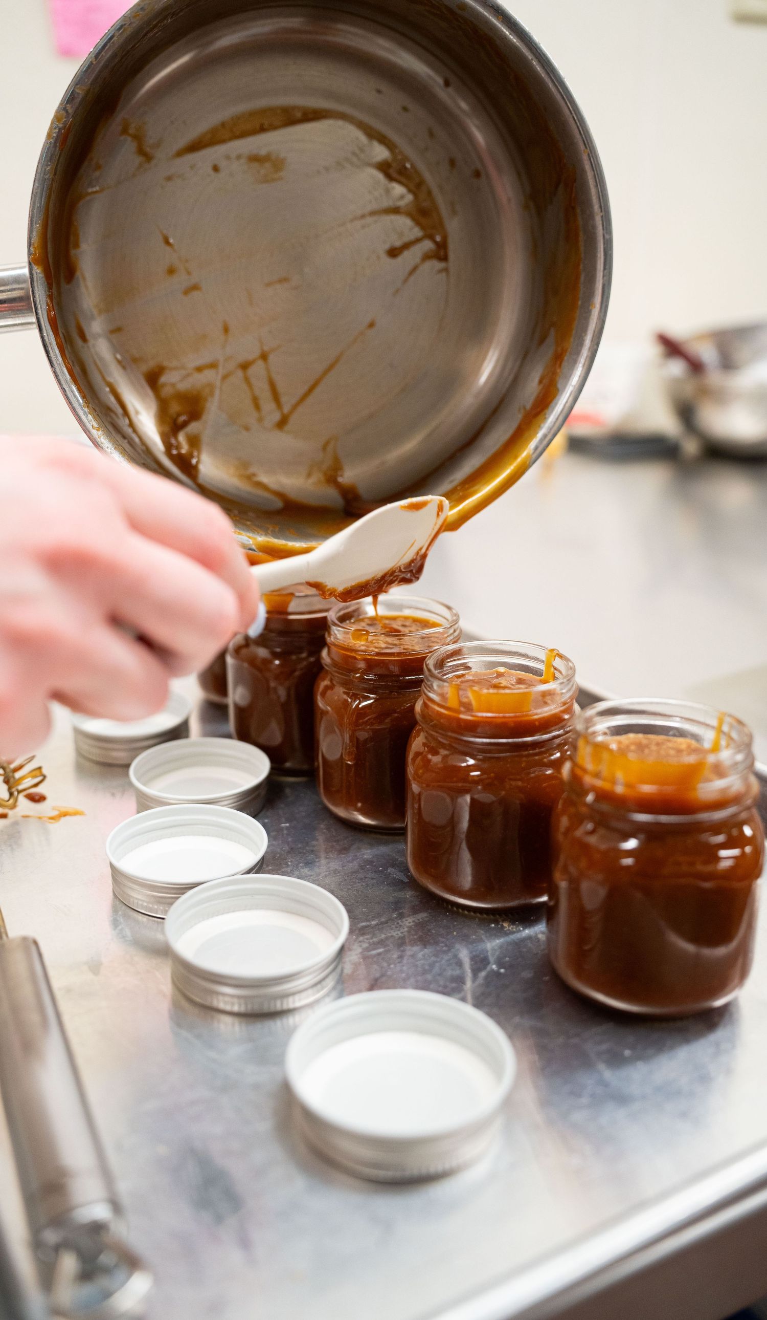 Pouring caramel sauce into small glass jars for packaging.