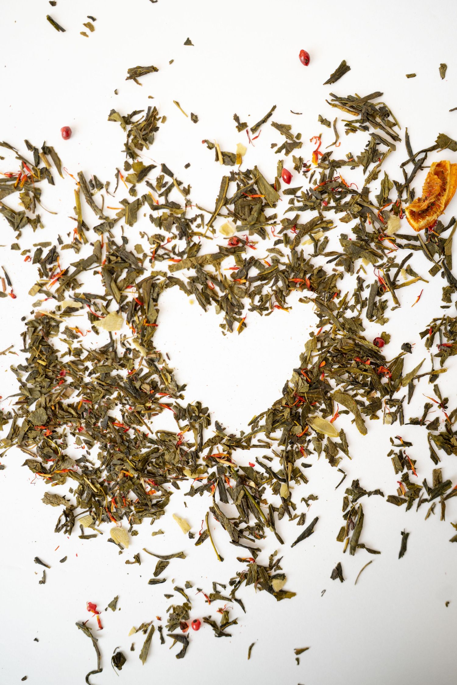 Dried tea leaves and flower petals arranged in a heart shape on white background.