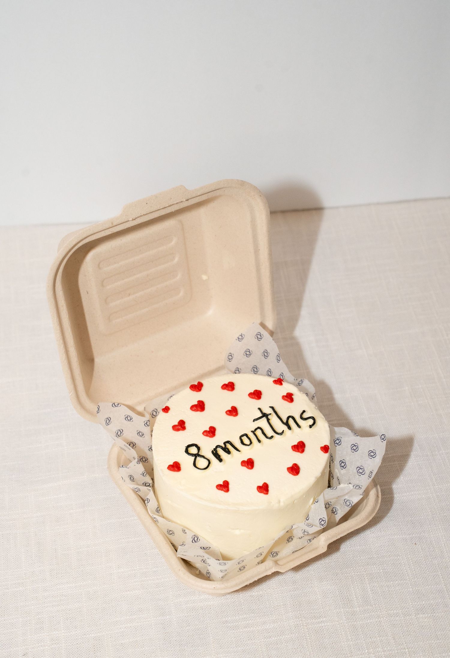 White celebration cake with red heart decorations and '8 months' text in a takeout container.