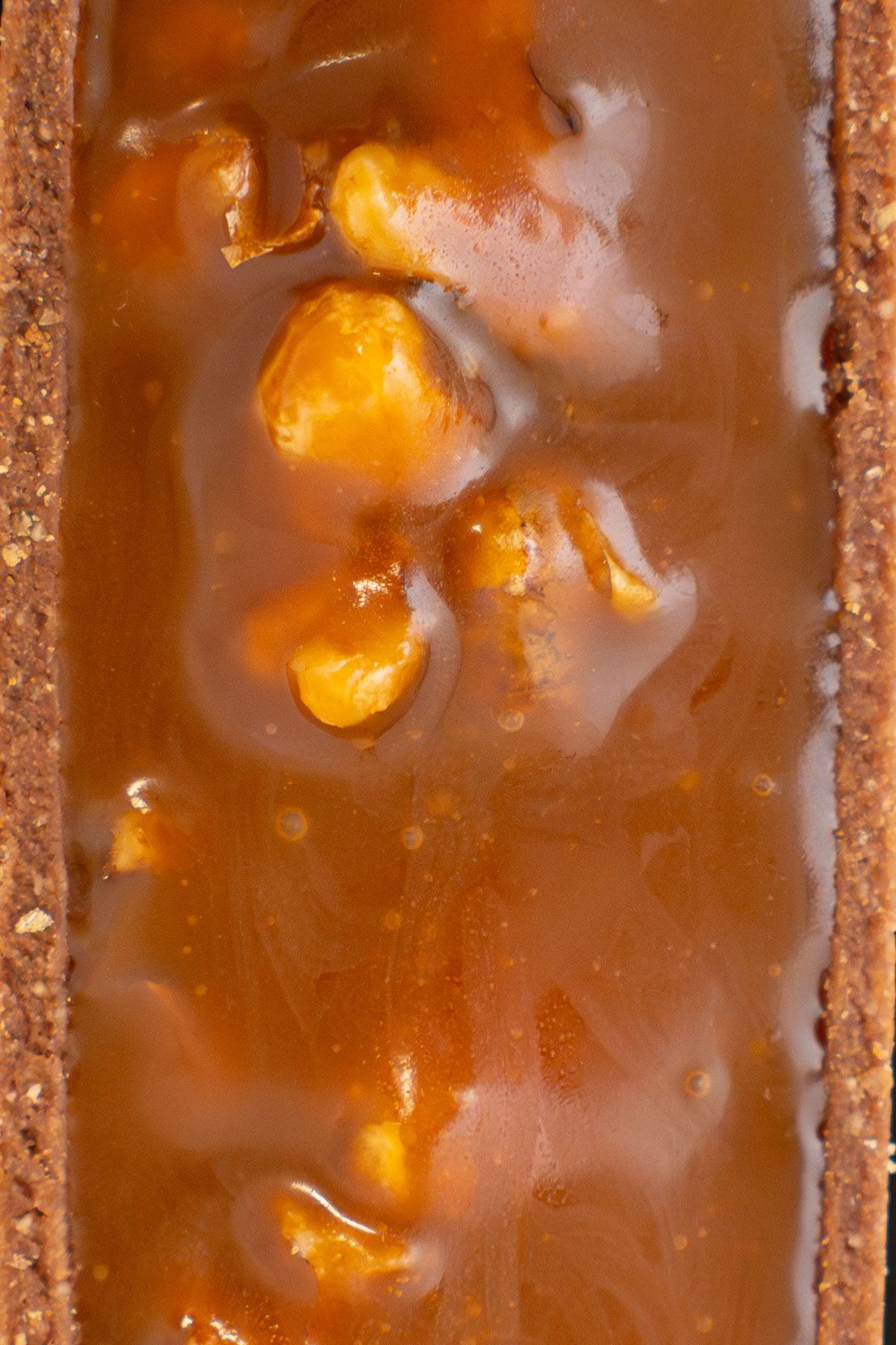 Close-up of caramel and nuts filling in a chocolate dessert bar.