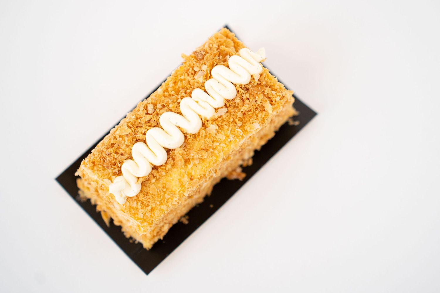Golden rectangular pastry topped with white cream piping on black plate.