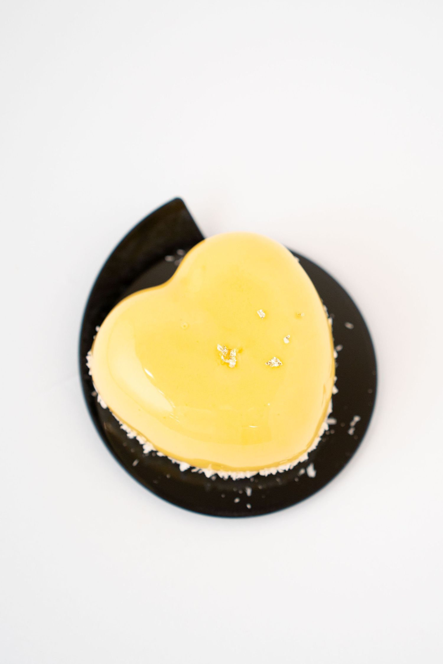 Heart-shaped yellow dessert on a black plate with a minimalist presentation.
