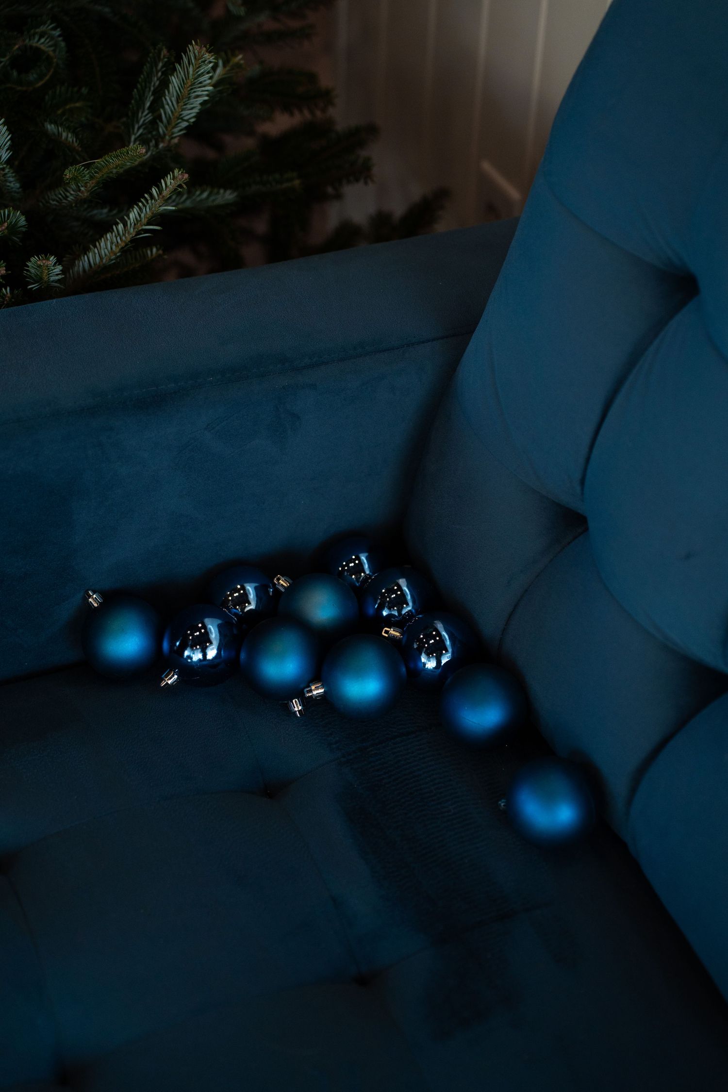 Blue Christmas ornaments scattered on a dark blue velvet couch in low light.