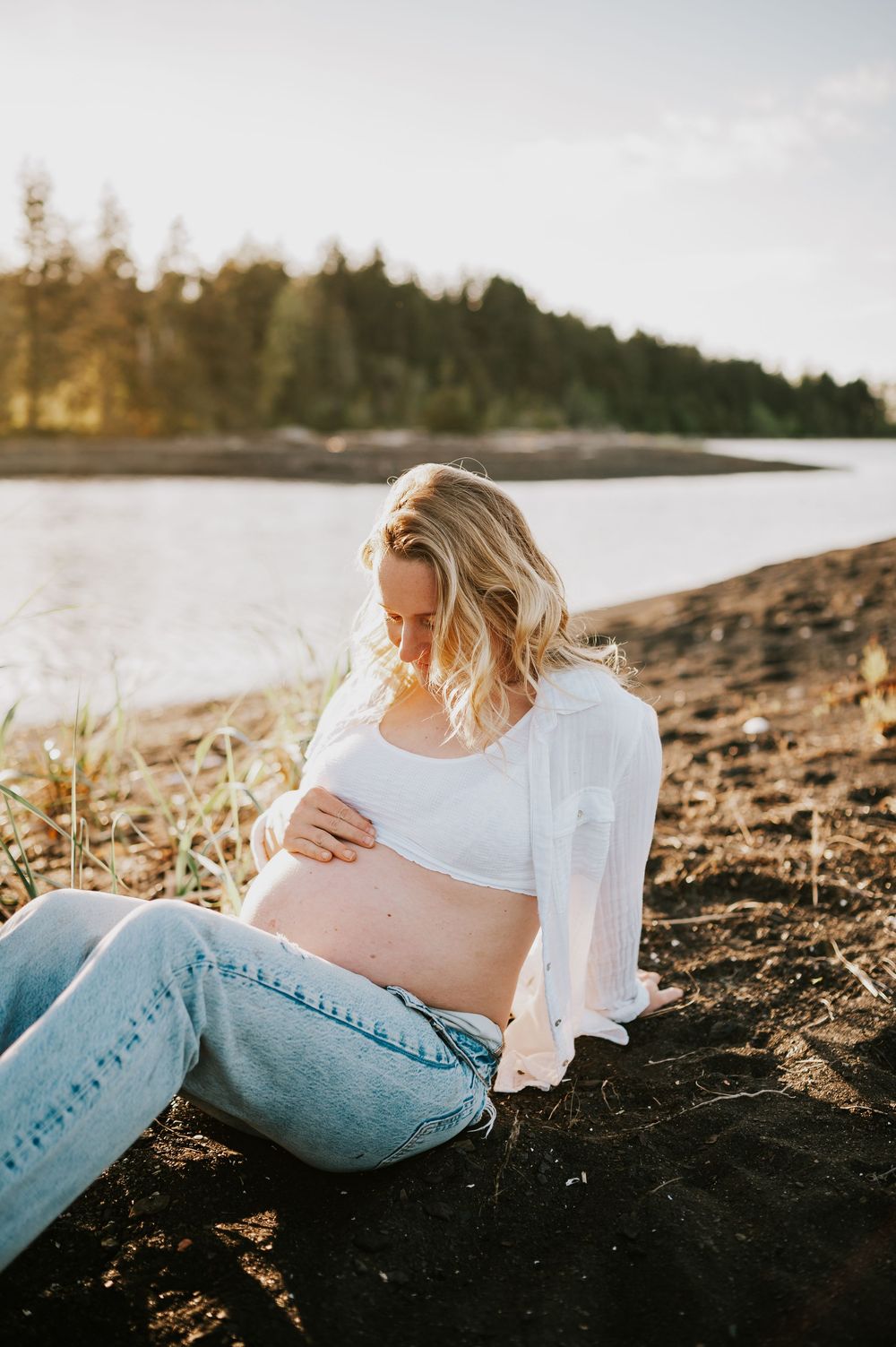 Sunset maternity photoshoot of woman holding pregnant belly sitting in Comox Valley beach. Photography by Photographer Soulfull Photographs