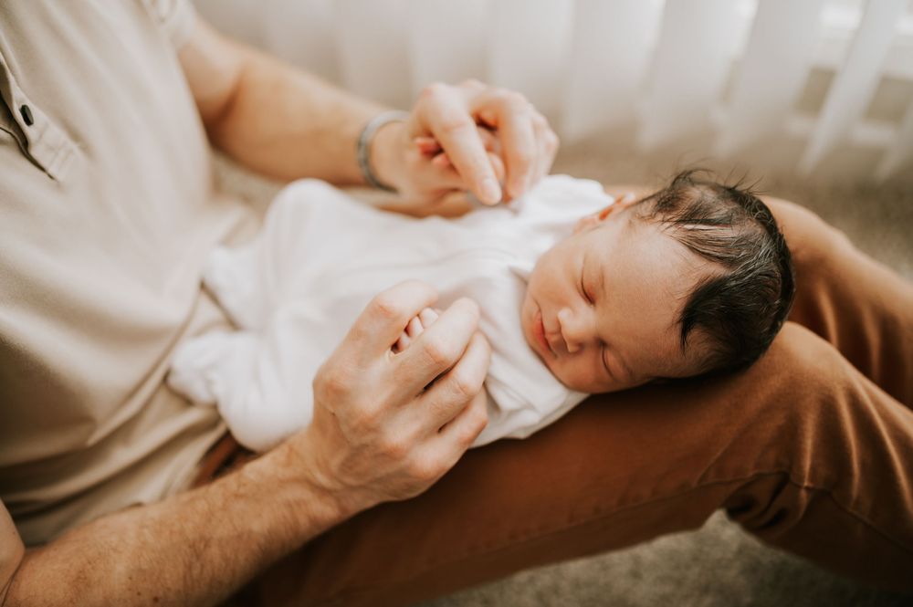 Little newborn baby sleeping portrait in home photoshoot in the Comox Valley on dads lap. Photography by Photographer Soulfull Photographs