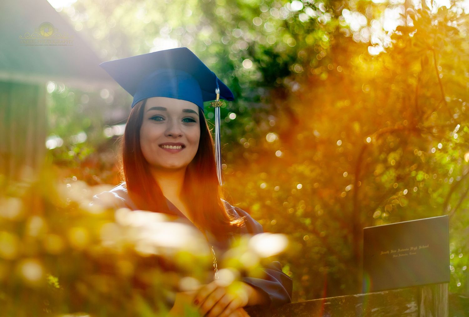 Graduate in traditional cap and gown posing outdoors in a park setting.