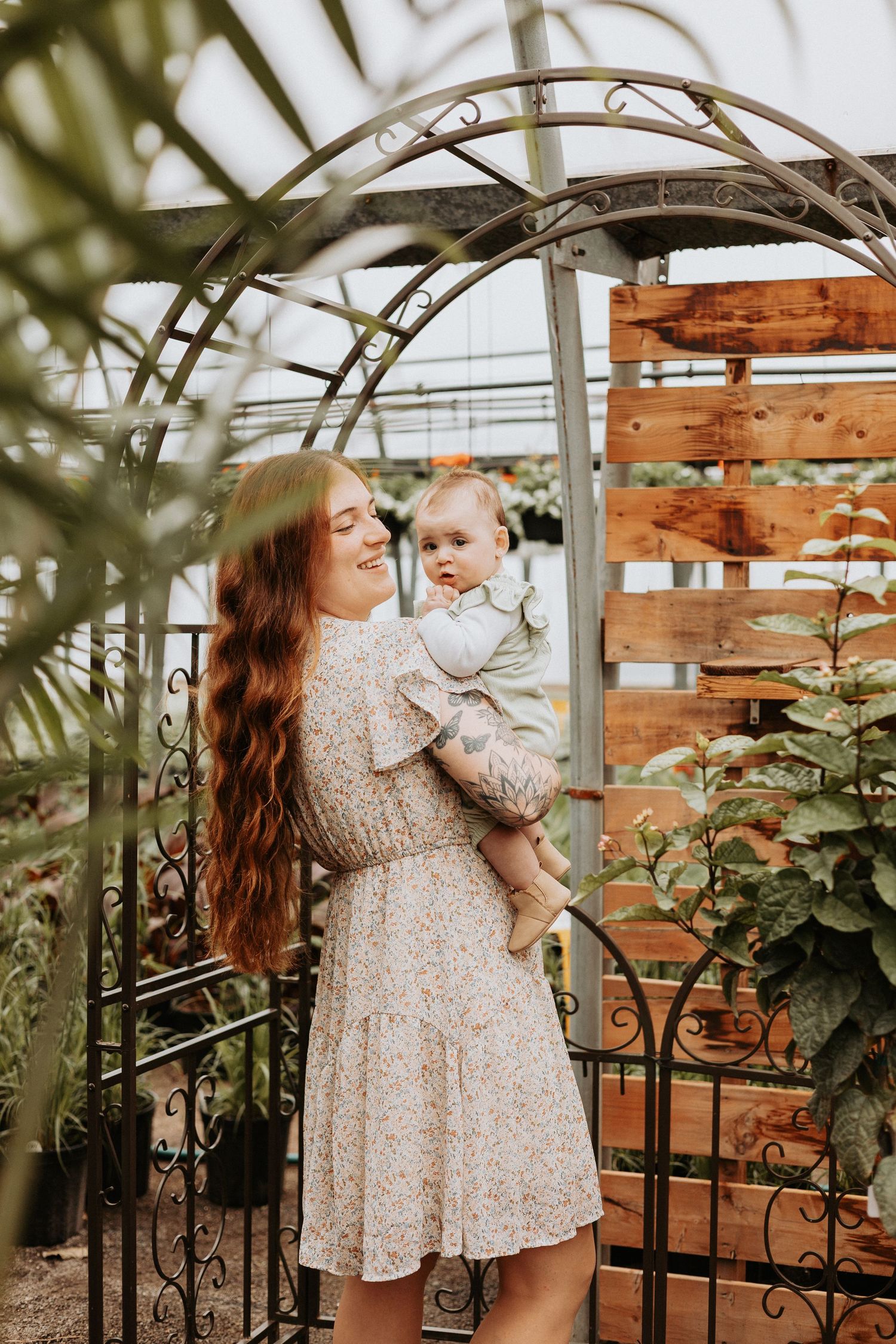 Two people in matching floral dresses share a tender moment together in a greenhouse setting with wooden decor.