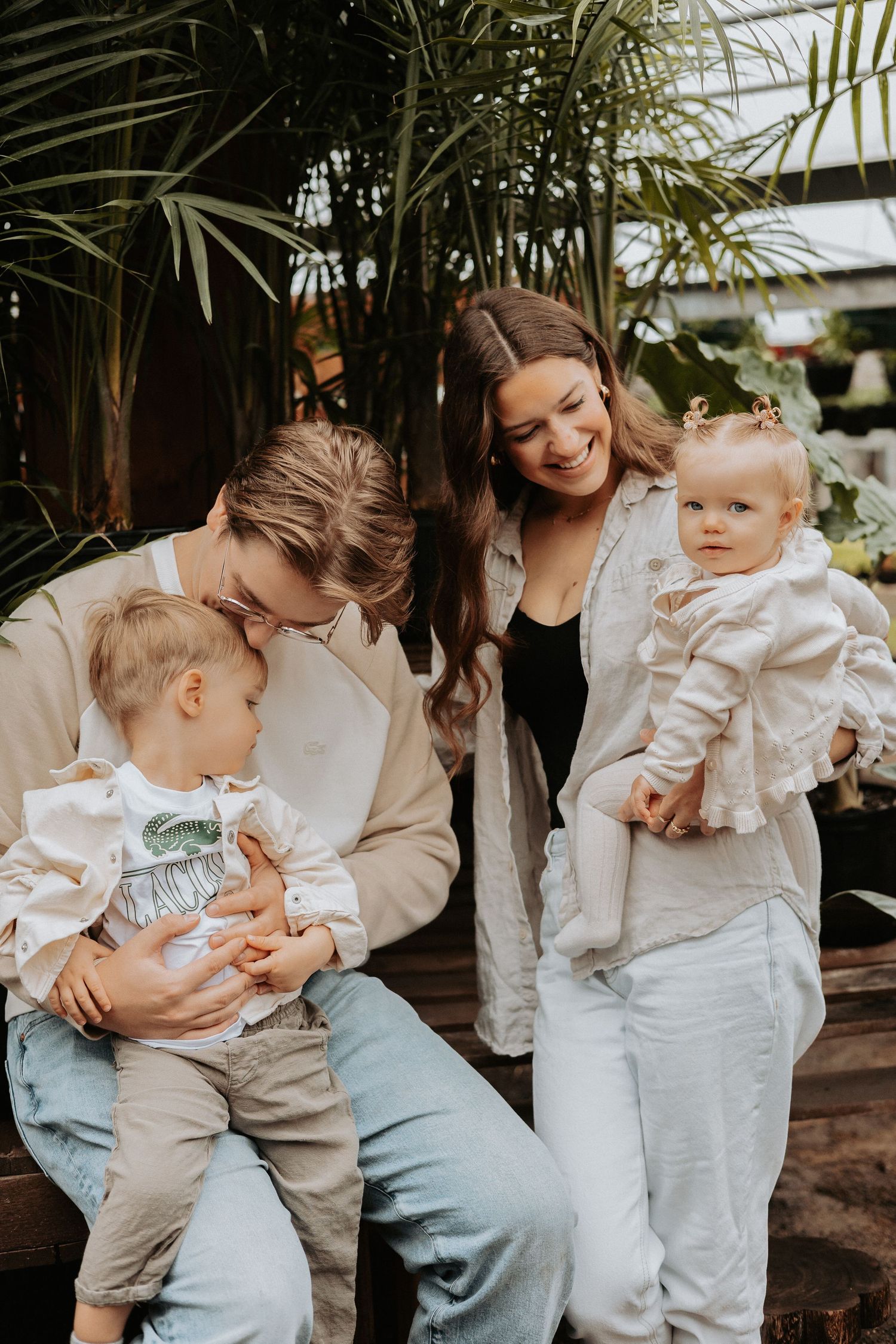 A family in casual attire shares a joyful moment together near tropical palm plants in an outdoor setting.
