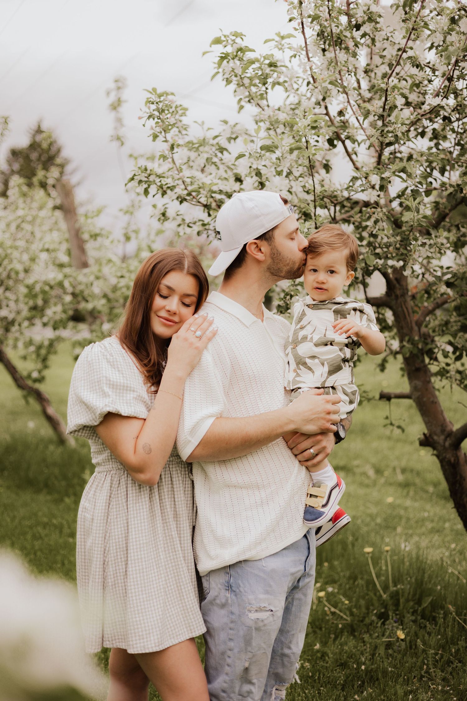 Family enjoying a spring day together in a blooming apple orchard wearing white outfits.
