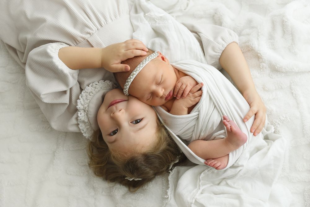 A baby wearing white clothing lies peacefully on soft white bedding while sleeping.