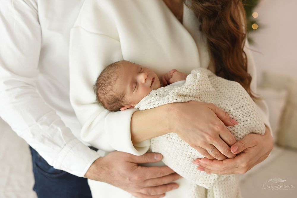 A series of tender moments showing hands gently cradling a newborn baby in white clothing.