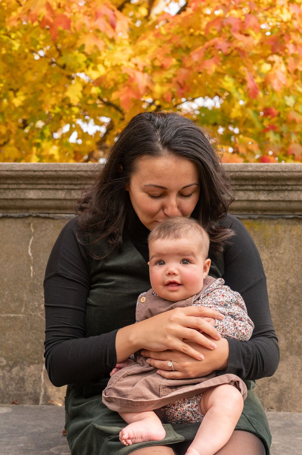 A tender moment between parent and baby against a backdrop of vibrant autumn foliage.