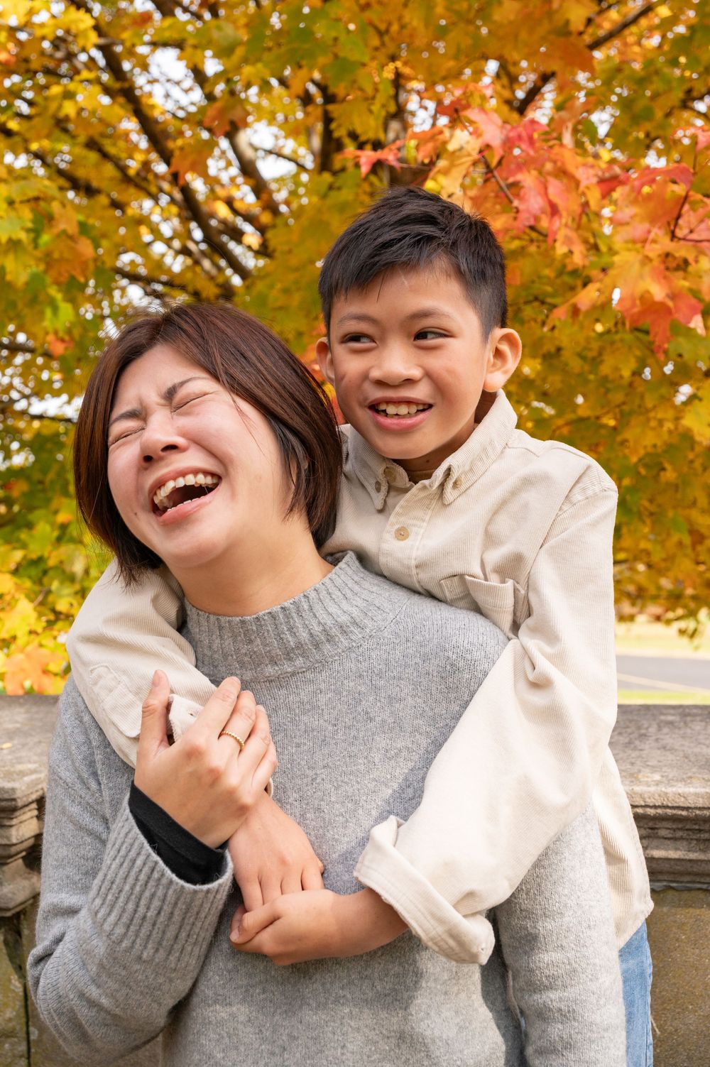 Two people share joyful laughter while sitting together outdoors among vibrant autumn foliage.